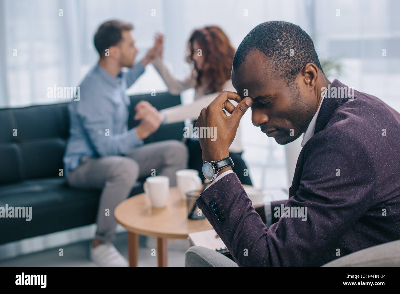 Tired african american psychiatrist in office with quarreling couple