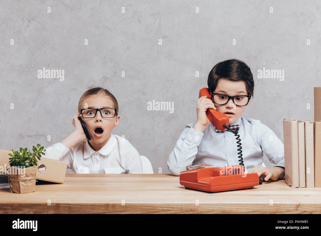 portrait of shocked children talking on smartphone and telephone while sitting at workplace Stock Photo