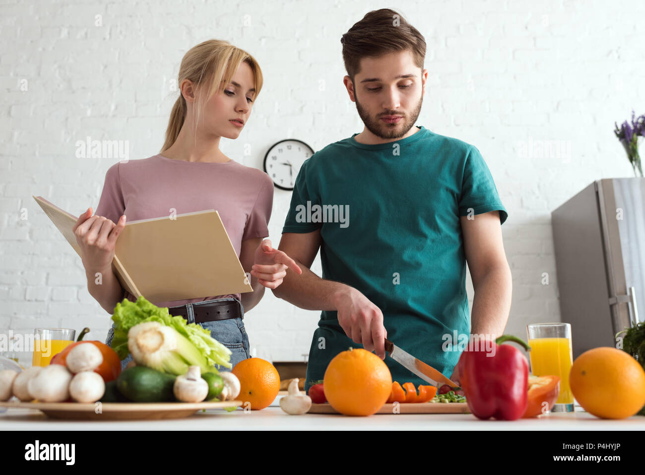 couple of vegans preparing food with recipe book at kitchen Stock Photo