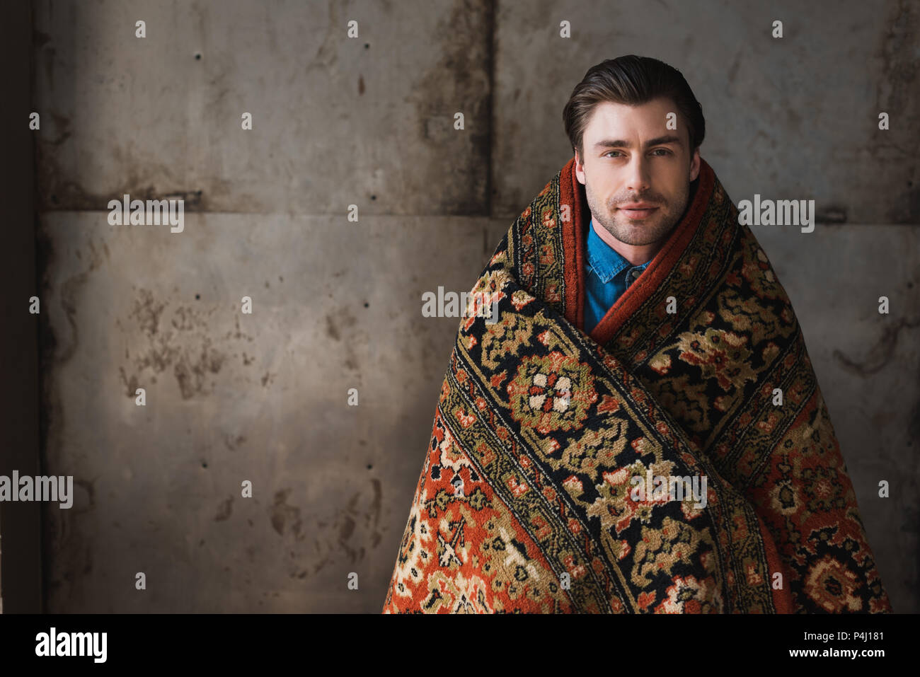 handsome young man covered in rug in front of concrete wall Stock Photo ...