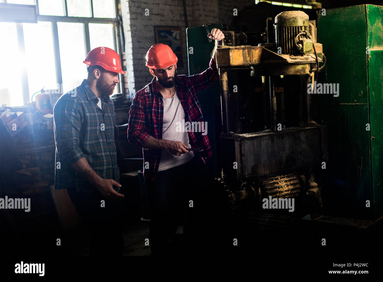 carpenters in protective helmets using machine tool at sawmill Stock Photo