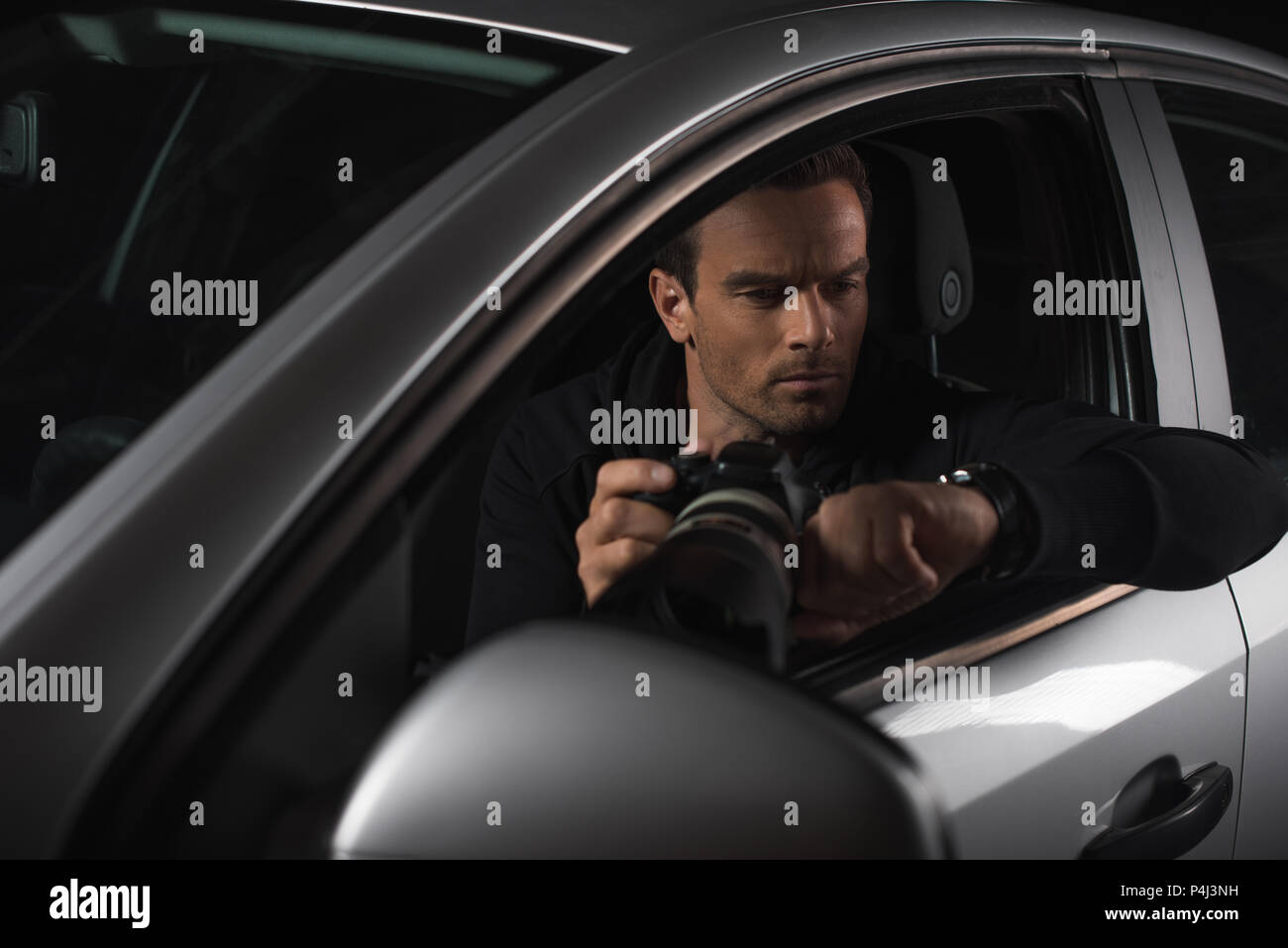 male paparazzi looking at wristwatch and spying by camera with lens from his car Stock Photo