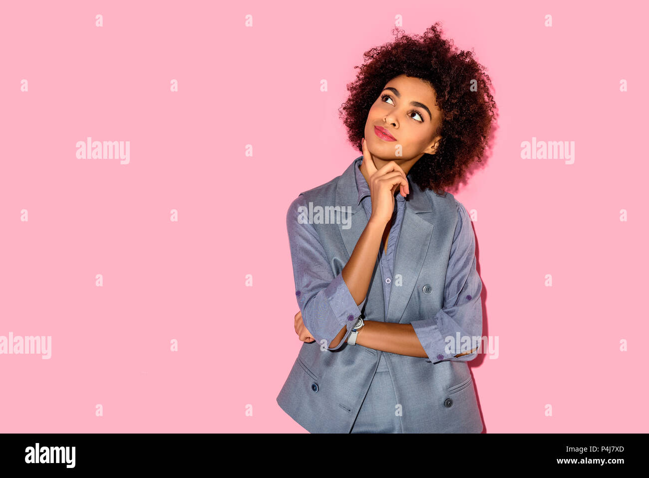 Young african amercian girl with hand on chin wearing grey suit on pink background Stock Photo