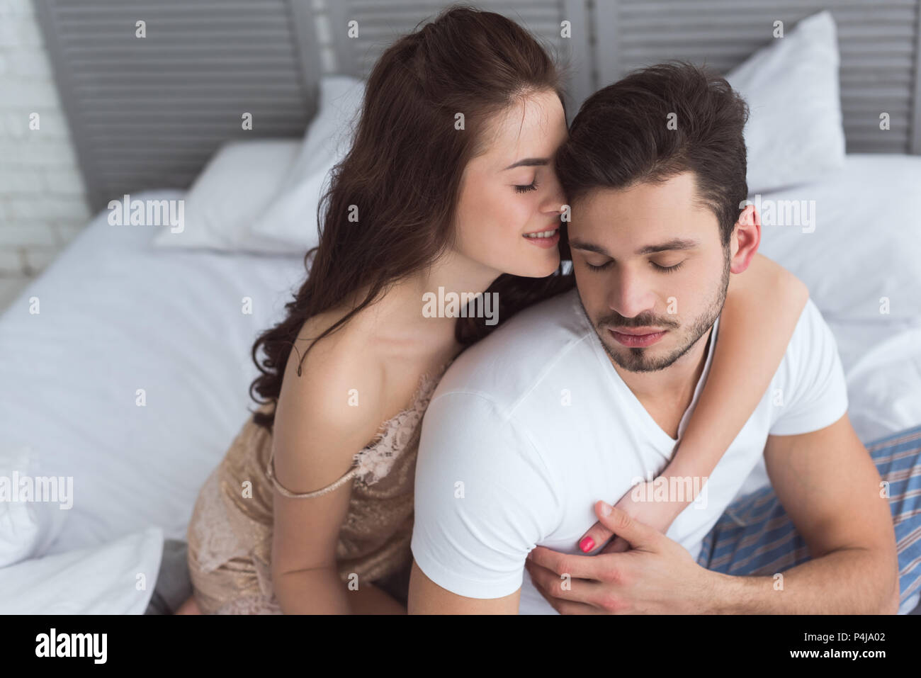 young woman in pajamas hugging boyfriend on bed at home Stock Photo - Alamy