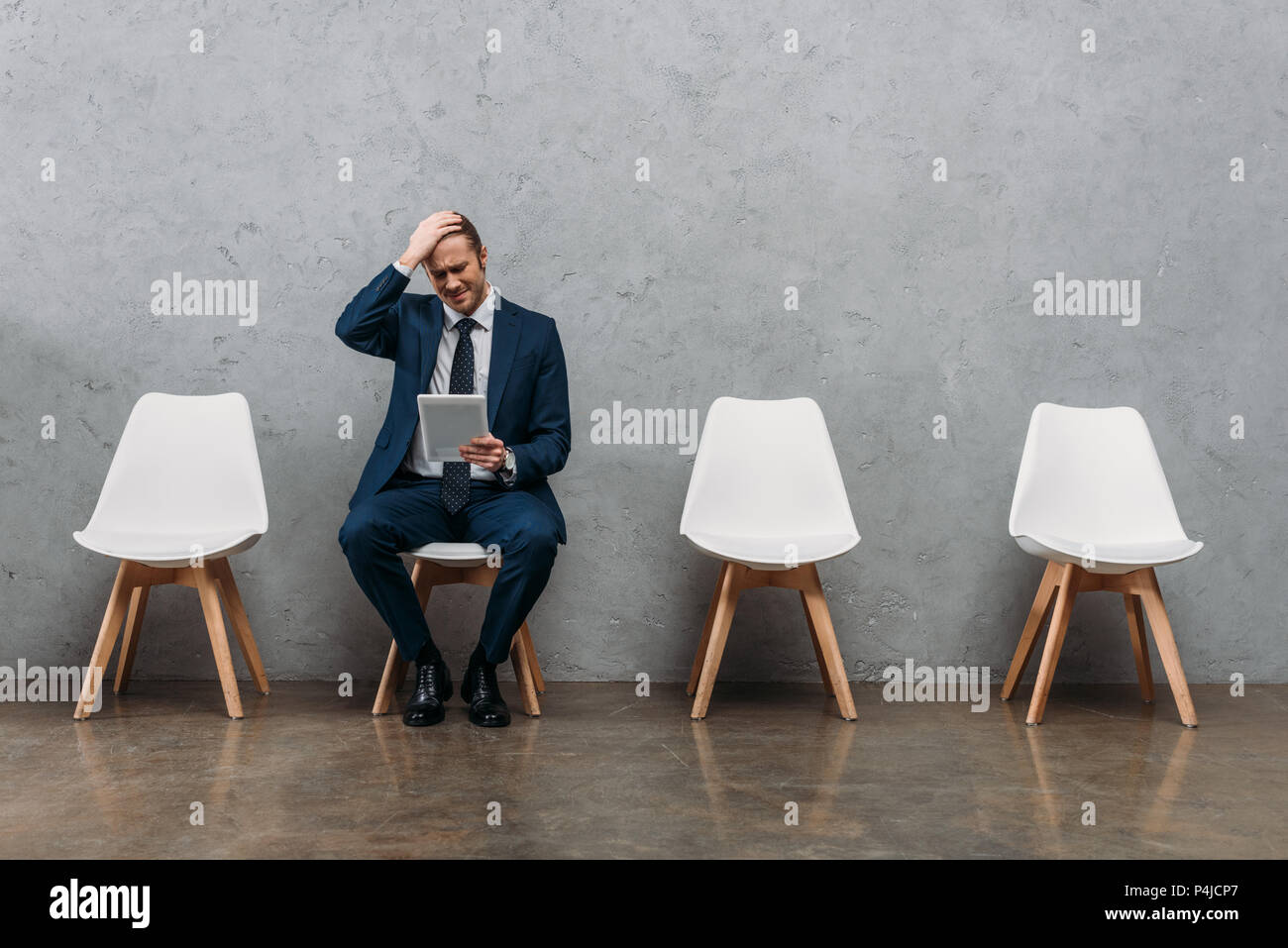 young frustrated businessman sitting on chair with tablet Stock Photo