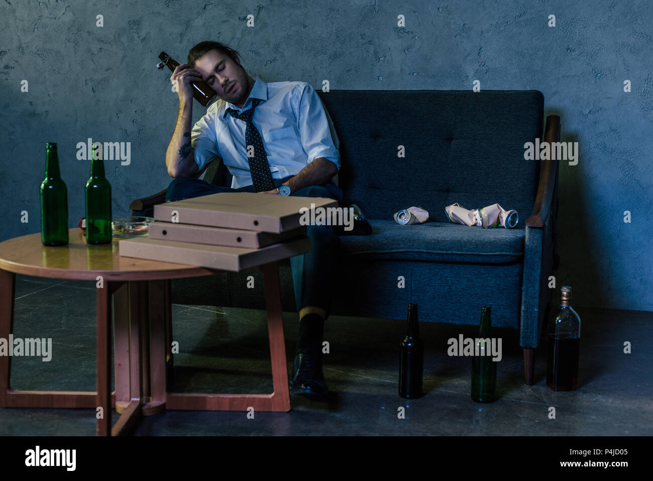 depressed alcohol addicted man drinking beer with pizza on couch after work Stock Photo