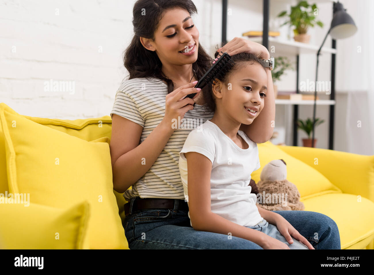 mother combing beautiful daughters hair on couch at home Stock Photo