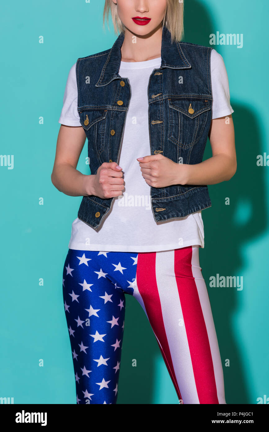 cropped shot of stylish woman in white shirt, denim jacket and leggings with american flag patternon blue backdrop Stock Photo