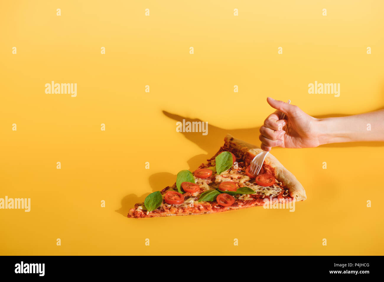partial view of woman sticking disposable fork into piece of pizza on yellow backdrop Stock Photo