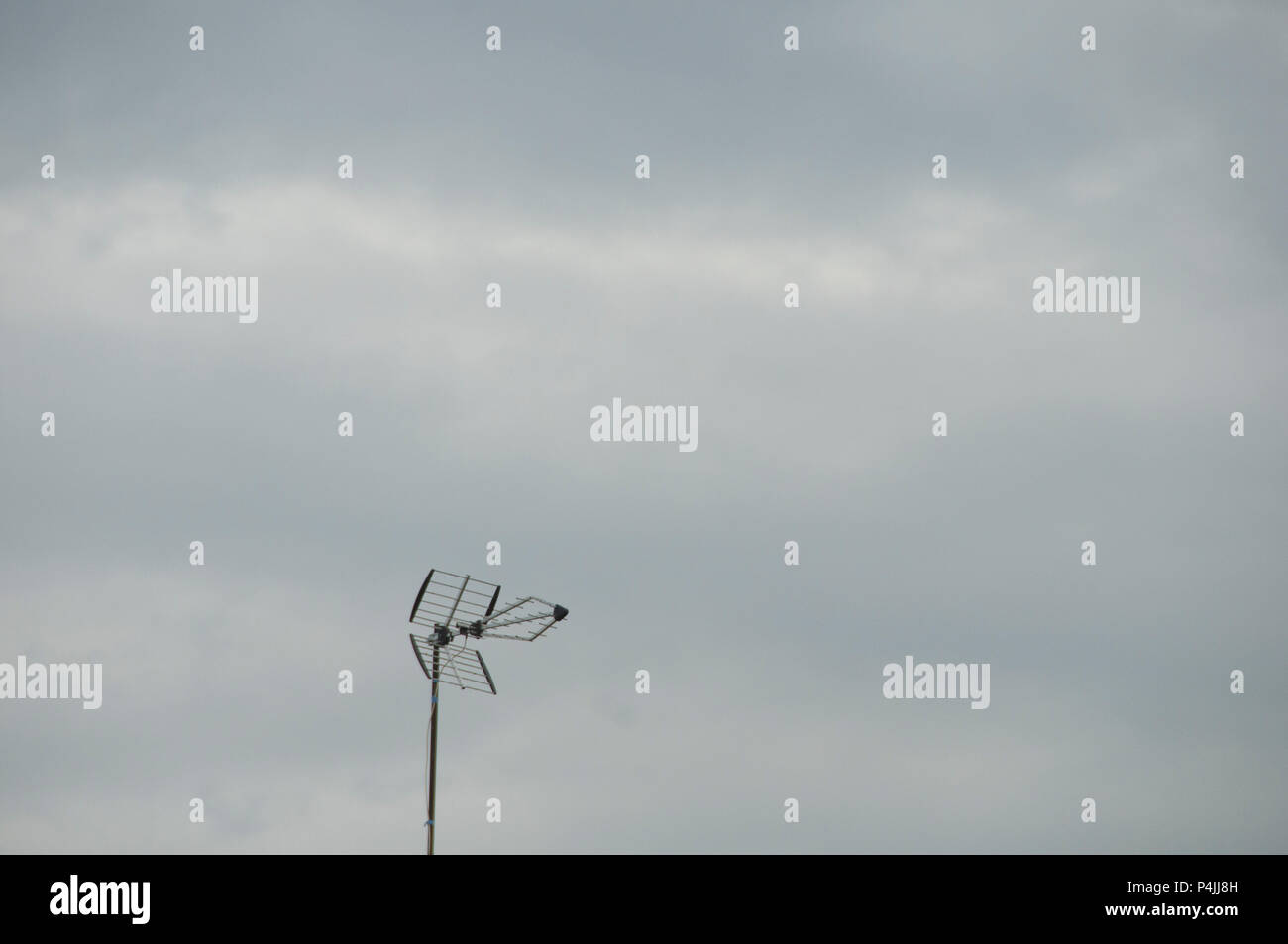 Old style TV aerial / antenna on top of black tiled roof against cloudy sky. Stock Photo