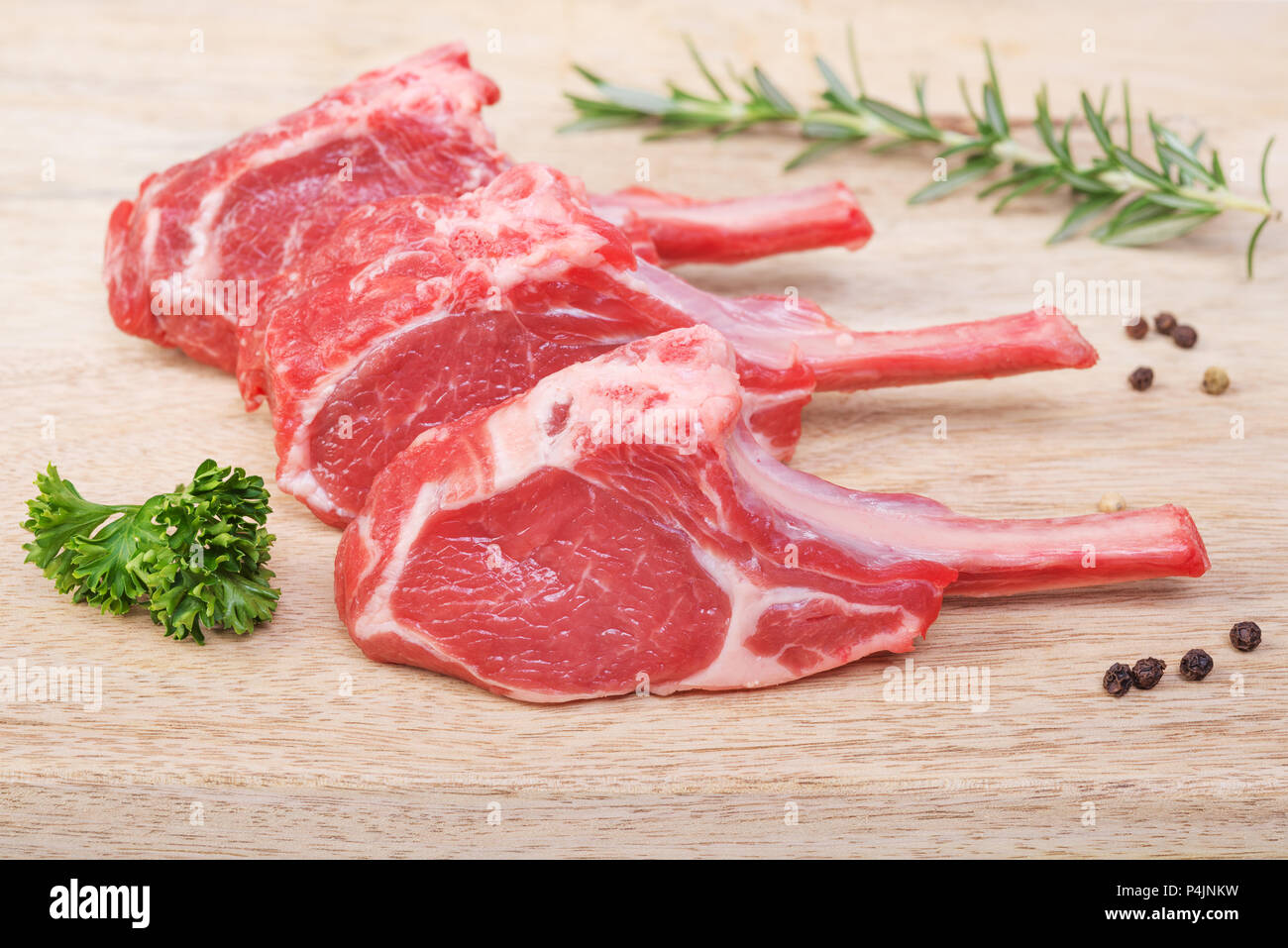 Fresh lamb cutlet  with  rosemary, parsley and pepper on light wooden  background. Stock Photo