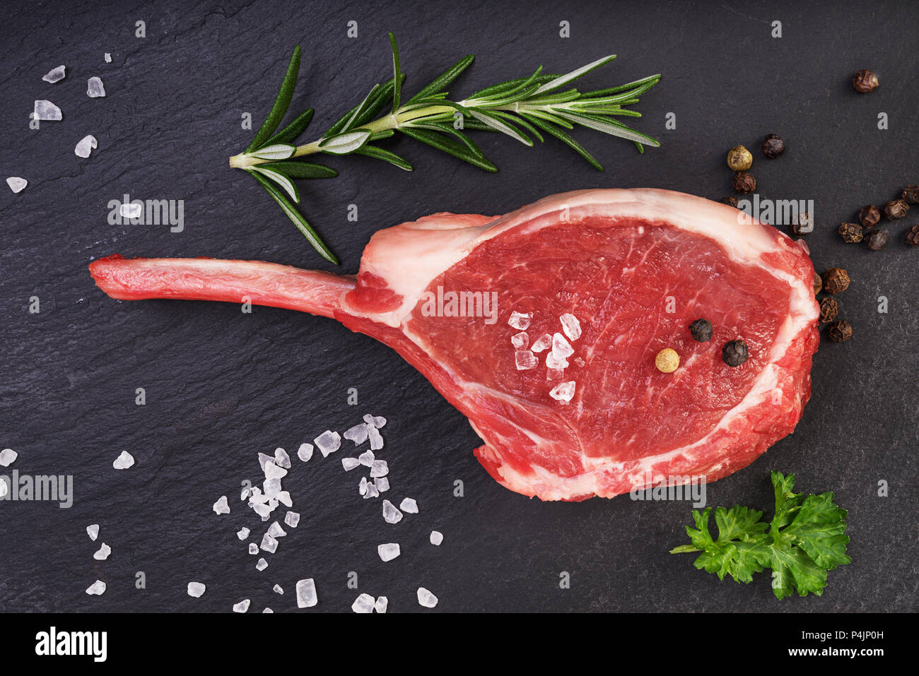 Fresh lamb cutlet  with  rosemary, pepper and salt on black stone  background. Meat ,top view Stock Photo