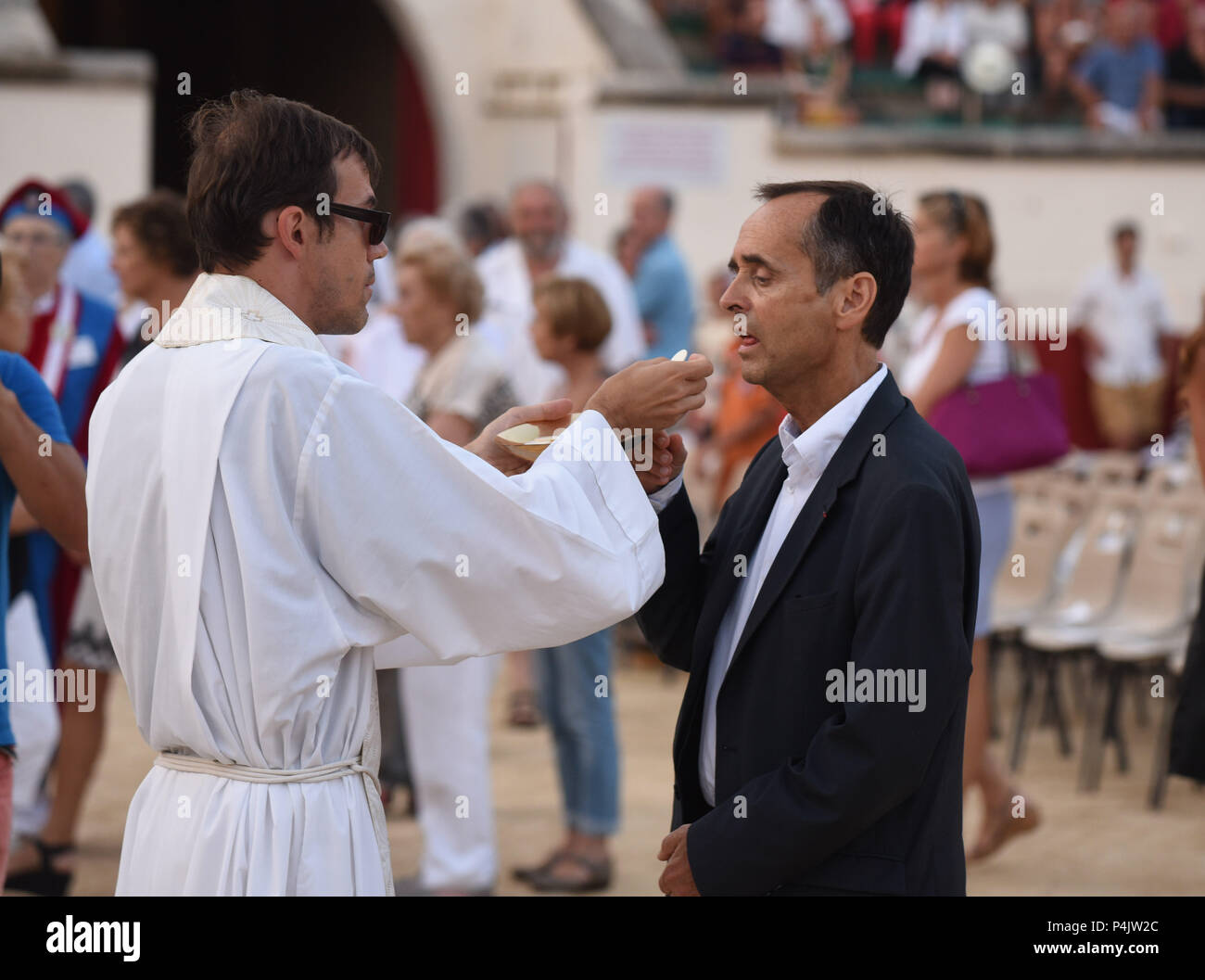 August 12, 2015 - Beziers, France: Beziers mayor eat sacramental bread during a Catholic mass in the bullfighting arena before the opening of the 'Feria', a summer festival of street parties and bullfighting. The town's new mayor, Robert Menard, has allowed the large public mass to take part in the arena as part of his municipal programme to reinvigorate the town's Catholic traditions. Le maire de Beziers Robert Menard recoit l'hostie pendant la messe en plein air dans les arenes de Beziers qui precede l'ouverture de la corrida. Stock Photo