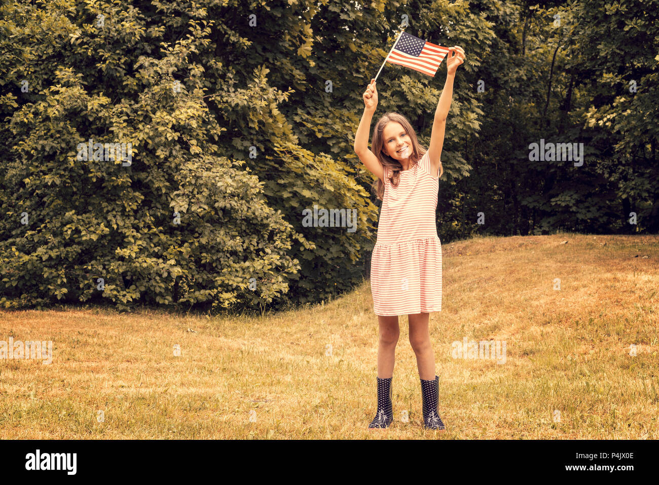 Happy girl with small american flag stands in park Stock Photo - Alamy