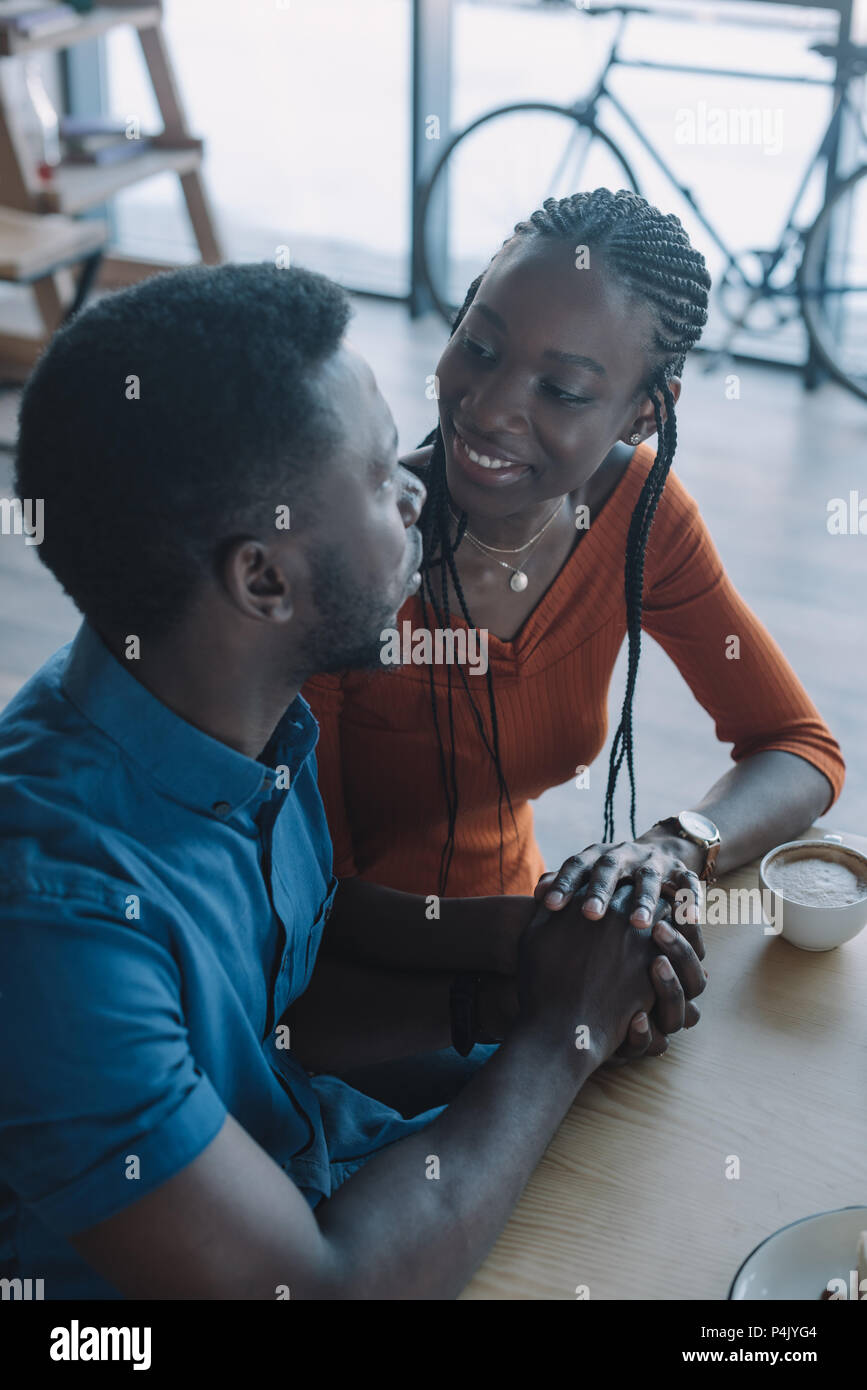smiling african american couple holding hands and looking at each other ...