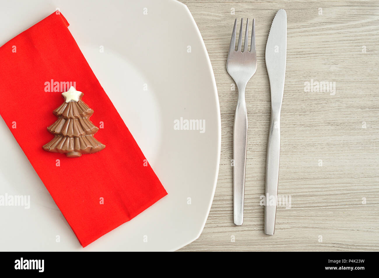 A simple place setting for Christmas consisting of a plate, fork, knife, red napkin and a chocolate shape christmas tree Stock Photo