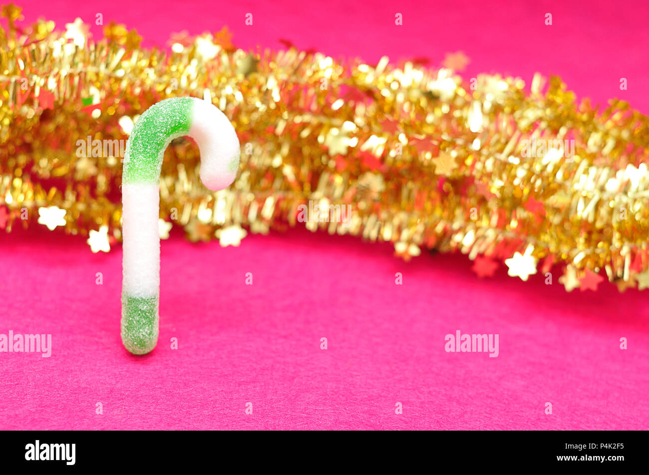 A green and white candy cane with golden tinsel against a pink
