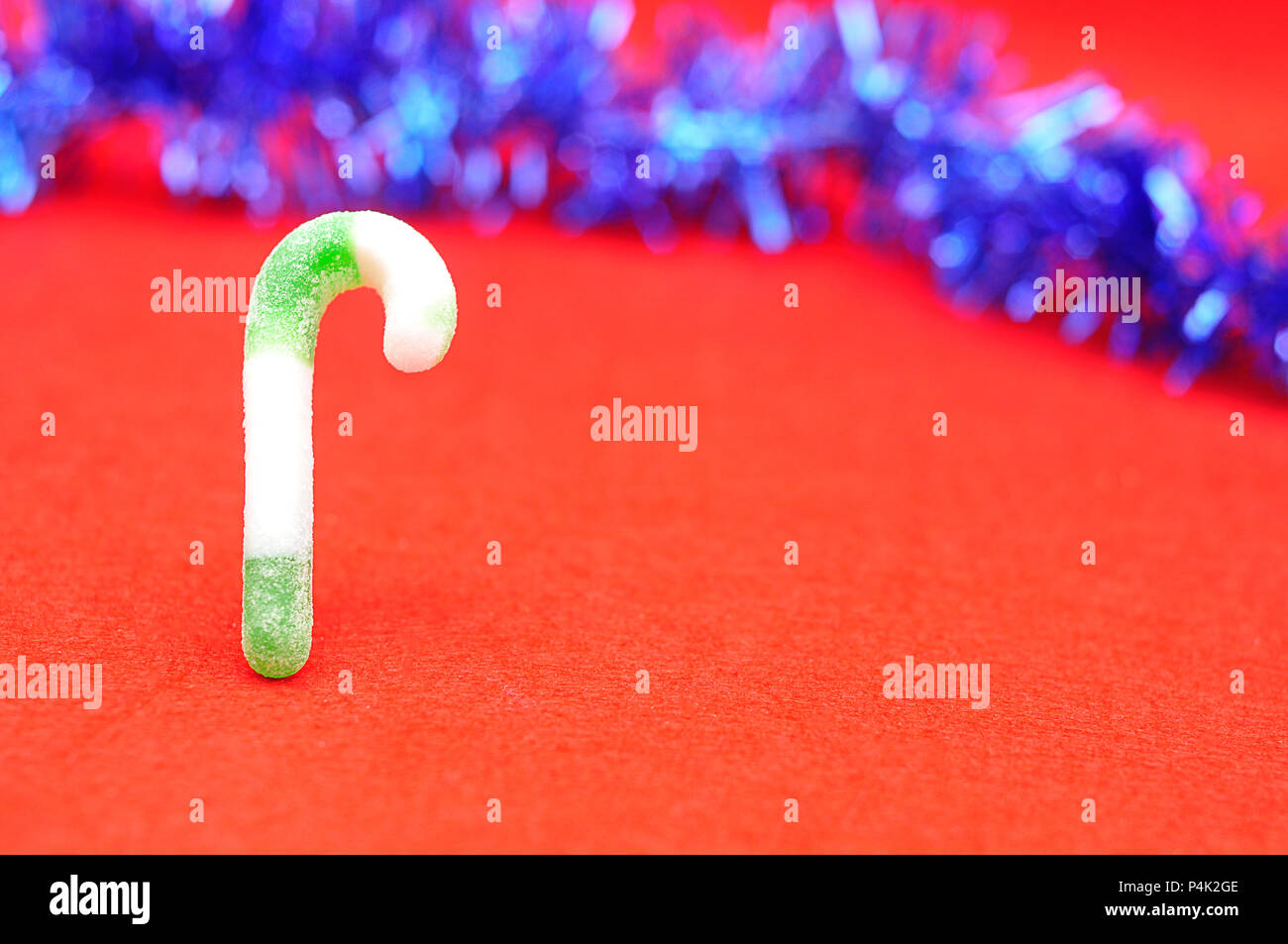 A green and white candy cane with blue tinsel against a red background