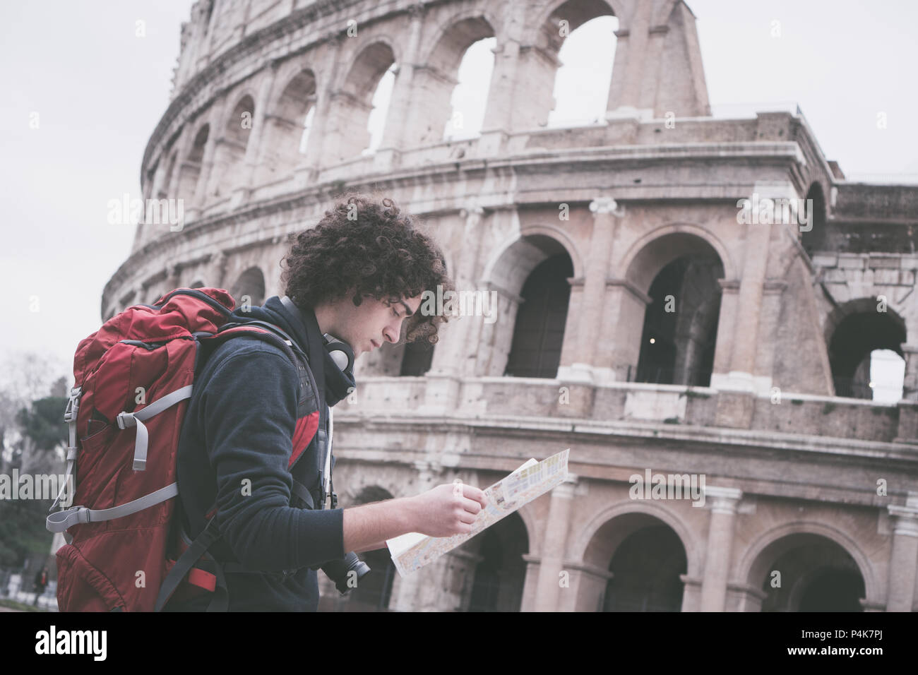 Vintage looking image of handsome young traveler looking at tourist map in Rome in front of Colosseum. Backpacker with camera and tourist map Stock Photo