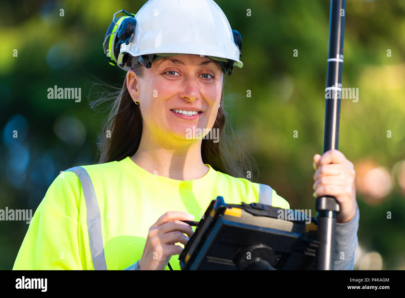 Woman in reflective clothing smiling while using GPS land surveying tool with screen Stock Photo