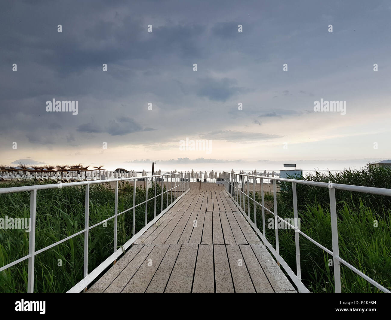 Wooden bridge as trail to the beach in a cloudy summer day before rain. Stock Photo