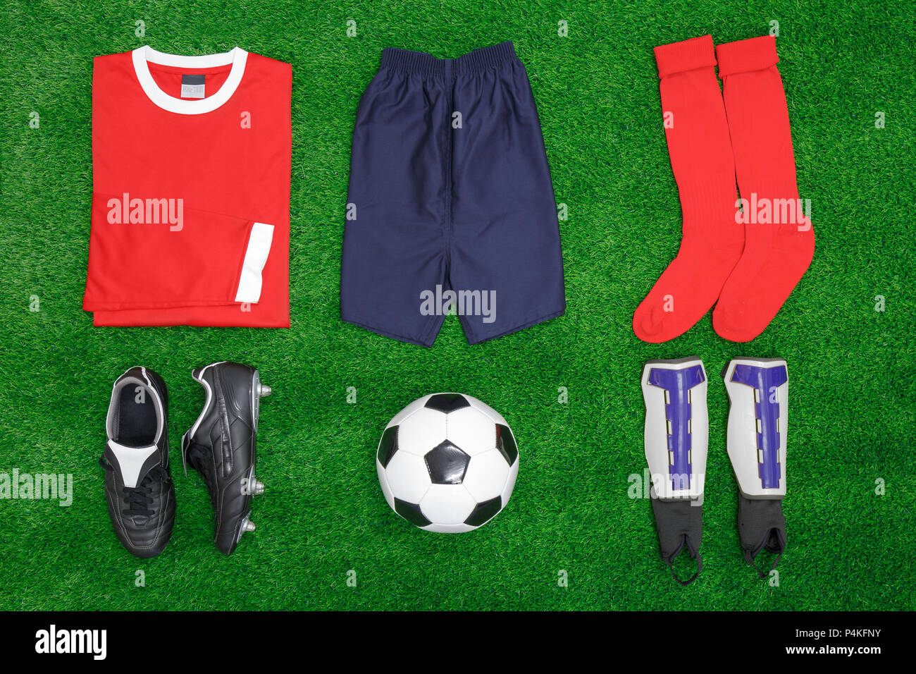 A flat lay arrangement of football or soccer kit on grass, with shirt, shorts,socks, boots, shin pads and ball. Stock Photo