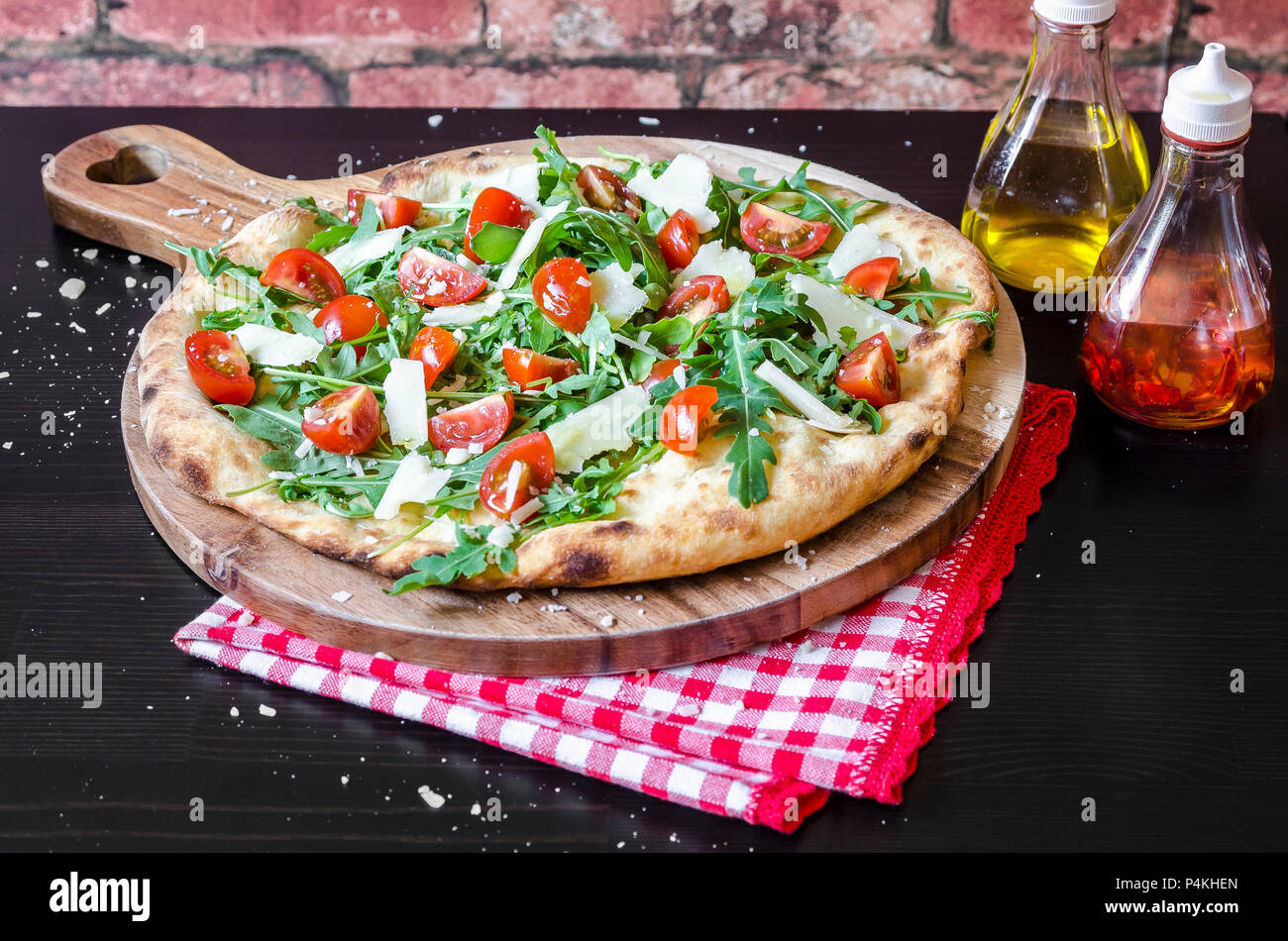 Pizza made with a sourdough base, fresh rocket leaves, cherry tomatoes and parmigiano cheese on a wooden board Stock Photo