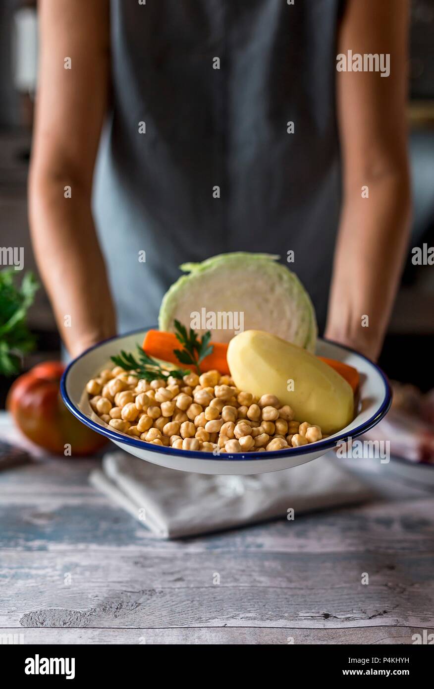 A woman holding a bowl of chickpeas, potatos, carrots and cabbage (ingredients for Cocido madrileno - a Spanish stew) Stock Photo