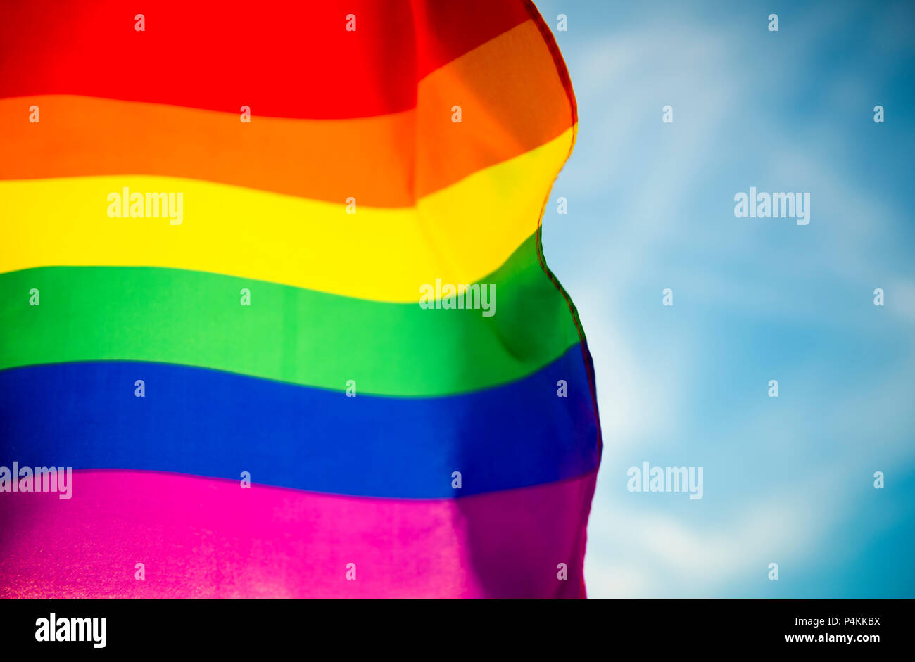 Backlit gay pride rainbow flag flutters in the breeze with lens flare ...