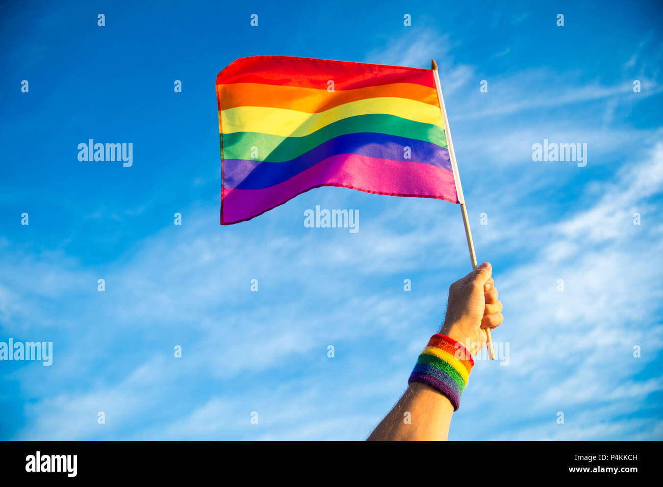 Colorful rainbow gay pride flag being waved in the breeze  by a hand wearing a sweatband Stock Photo