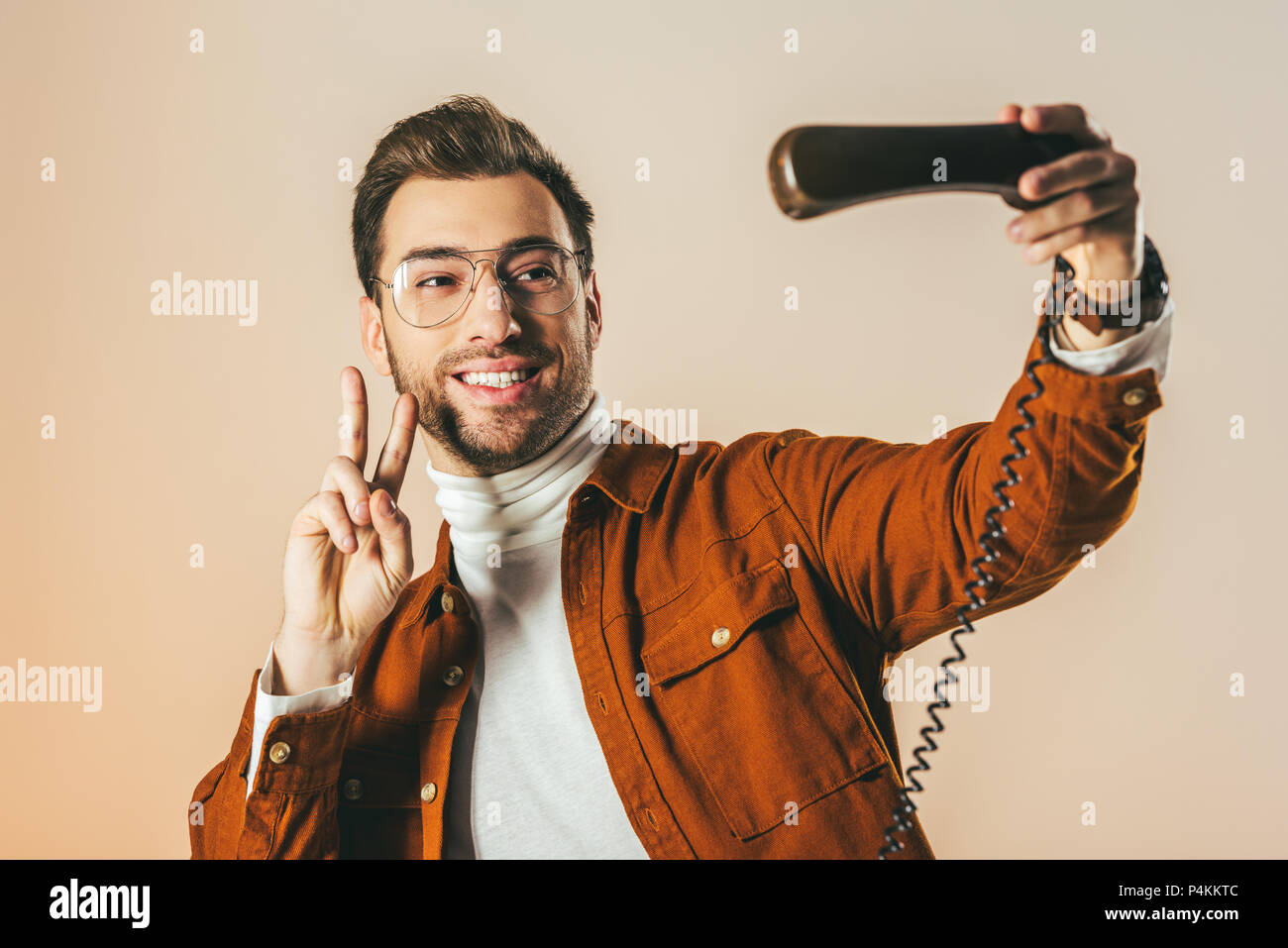 portrait of smiling man showing peace sign while pretending taking selfie in telephone tube isolated on beige Stock Photo