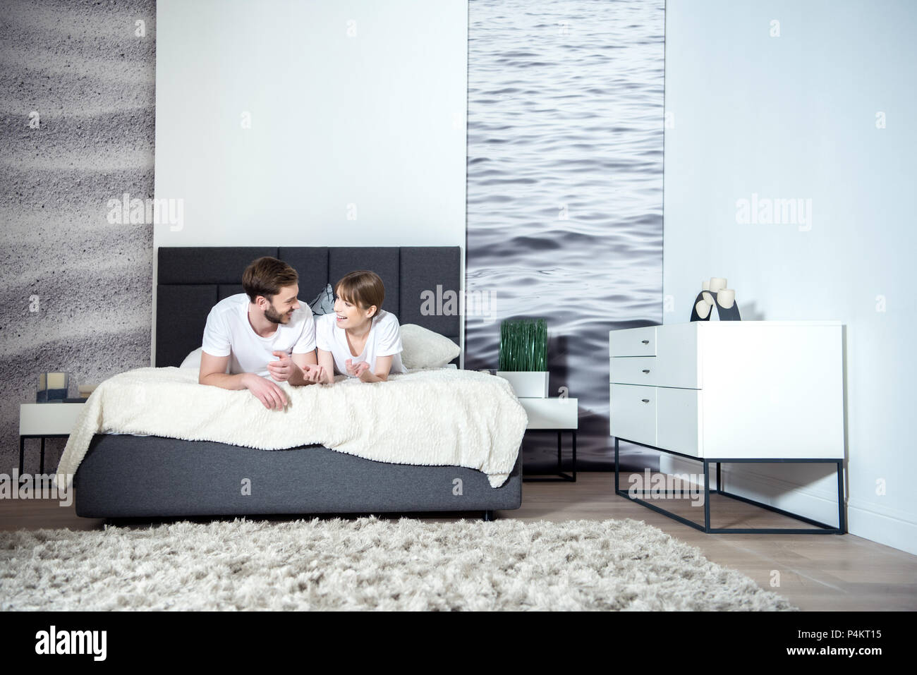Smiling Couple Talking And Lying On Bed In Cozy Bedroom With