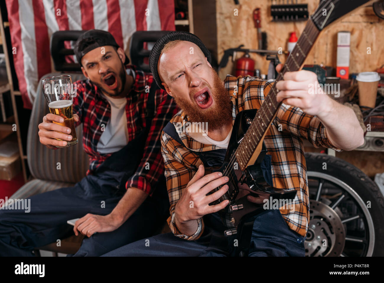 drunk mechanics playing guitar and drinking beer at garage Stock Photo