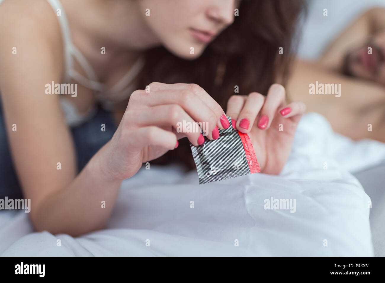 cropped shot of woman opening condom on bed Stock Photo