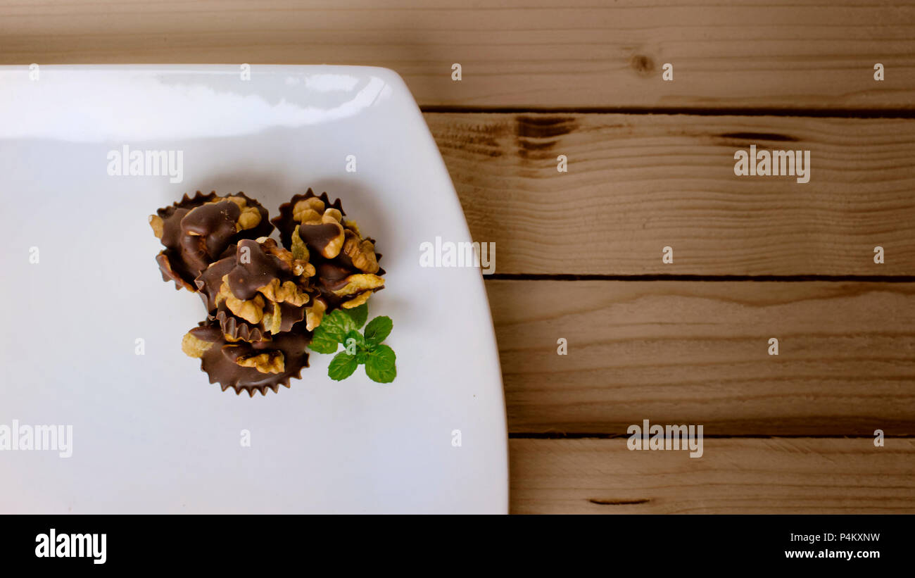 Walnuts and corn flakes covered in dark chocolate decorated with mint leaf on a wooden table Stock Photo