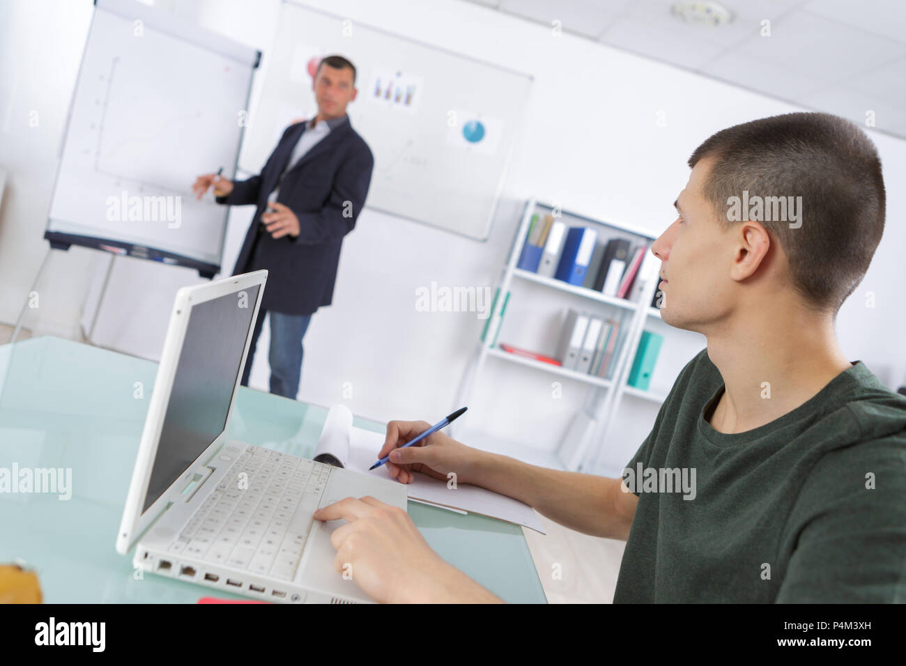 man stood at flipchart student sat using laptop making notes Stock Photo