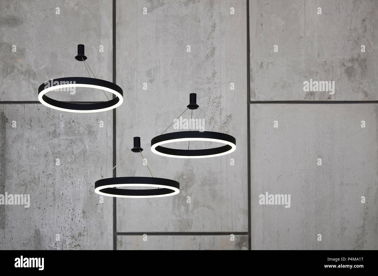 Unusual light sources hang on the background of a marble wall. Lamps in the form of a luminous ring . Stock Photo