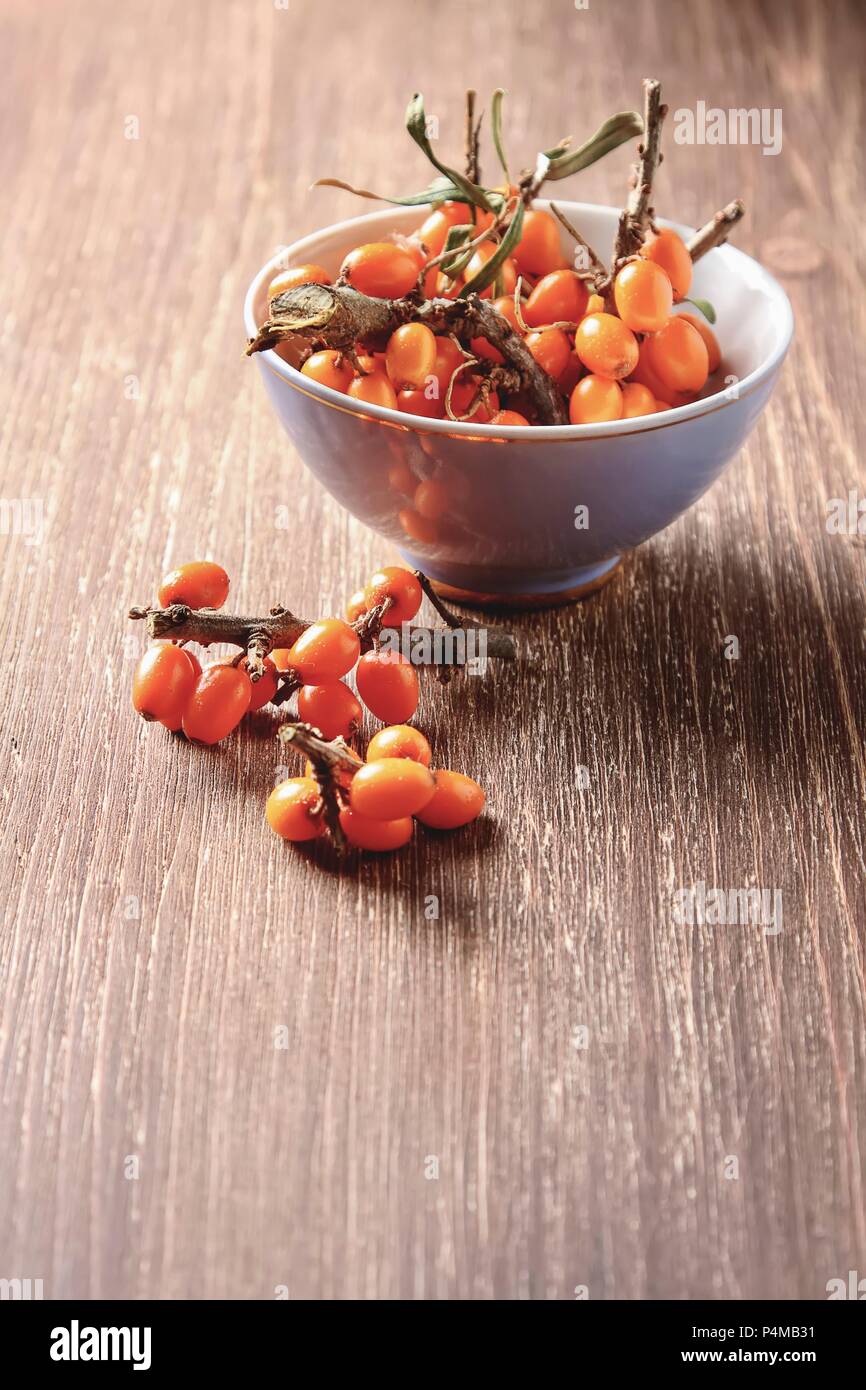 Fresh sea buckthorn in a bowl and next to it on a wooden surface Stock Photo