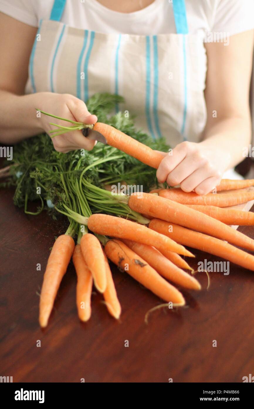 A woman removing the leaves from a bundle of carrots Stock Photo