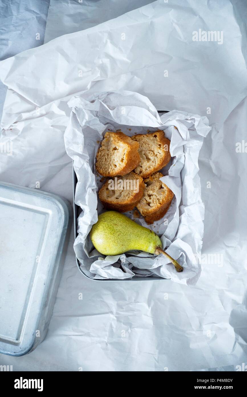 A lunchbox containing a pear and four pieces of vegan pear cake made of spelt and cornflour, sweetened with coconut blossom sugar Stock Photo