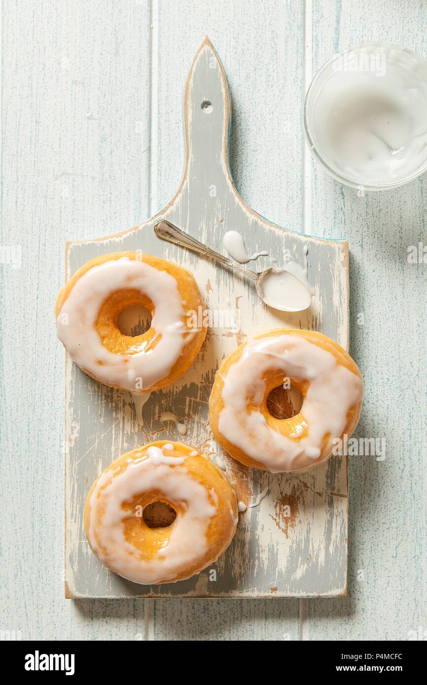 Three iced doughnuts on a grey wooden chopping board with a spoon Stock Photo