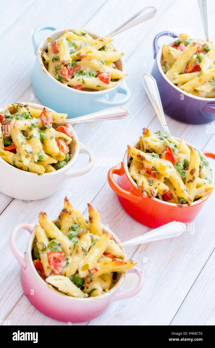 Mini servings of pasta bake with peas, cherry tomatoes in a creamy white sauce served in small colourful pots with forks Stock Photo