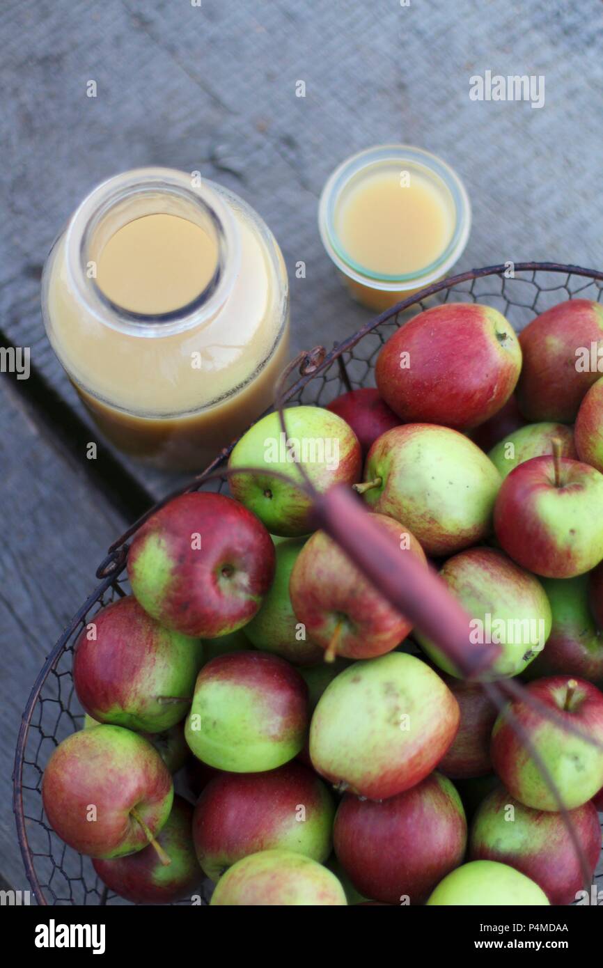 Fresh naturally cloudy apple juice in a glass and bottlenecks to a basket of apples Stock Photo