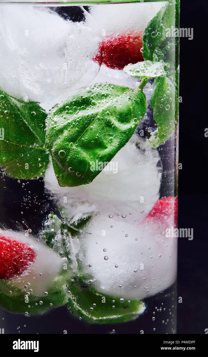 Ice cubes with raspberries and basil in a glass of water Stock Photo