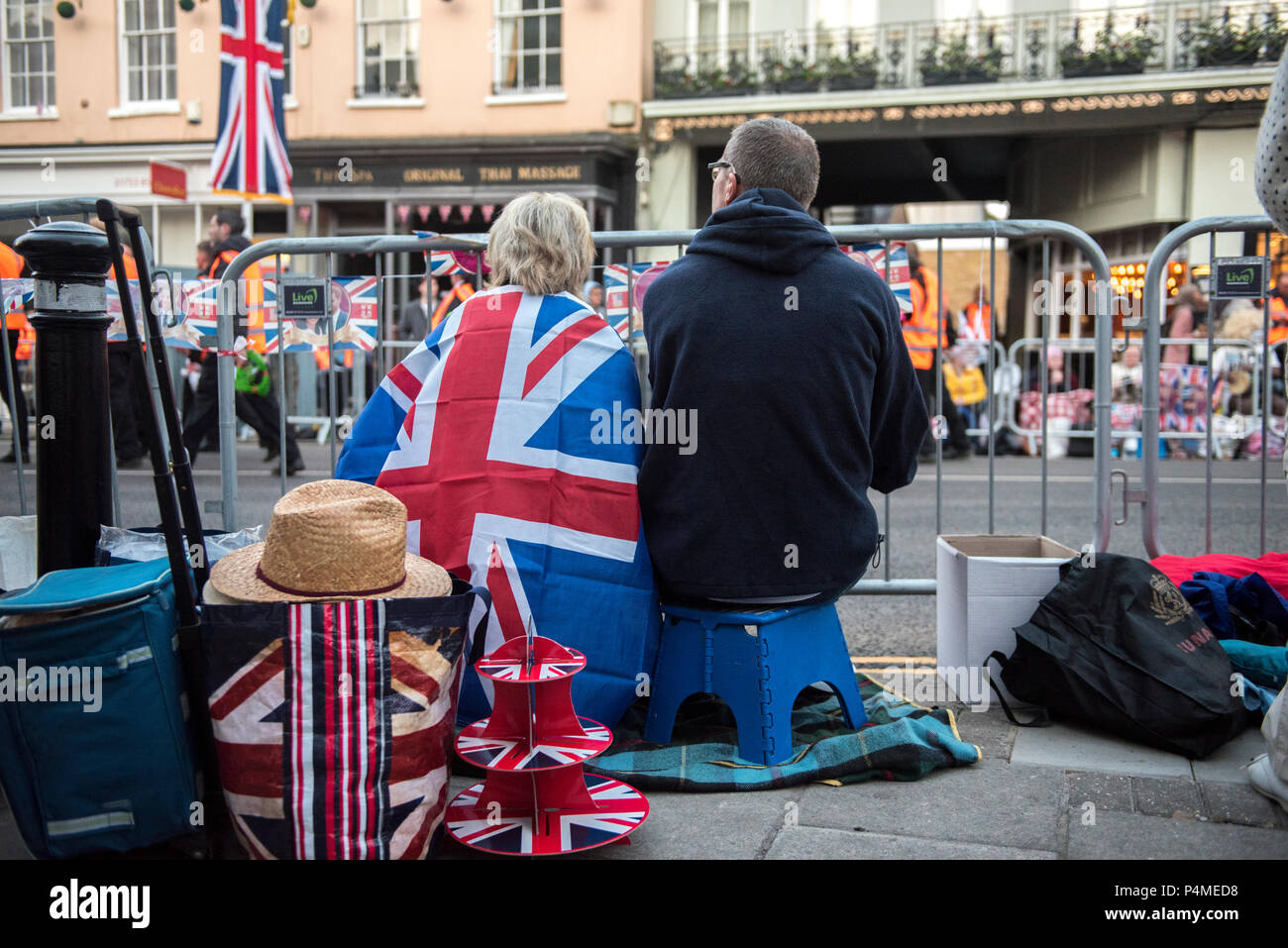 Two people awake early on the morning of the royal wedding of HRH Prince Harry and Ms. Meghan Markle. They sit up on steps and watch arriving volunteers and council workers walking along the streets of Windsor to take up positions for the event. Stock Photo