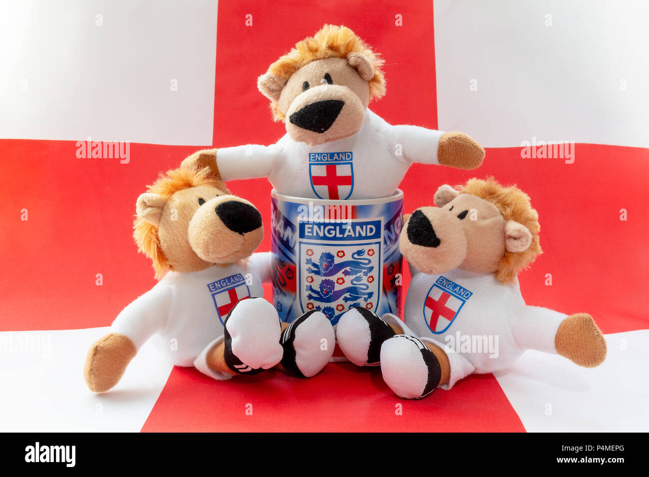 Three lions sit in and around an England mug with a St George's Cross flag as a background Stock Photo