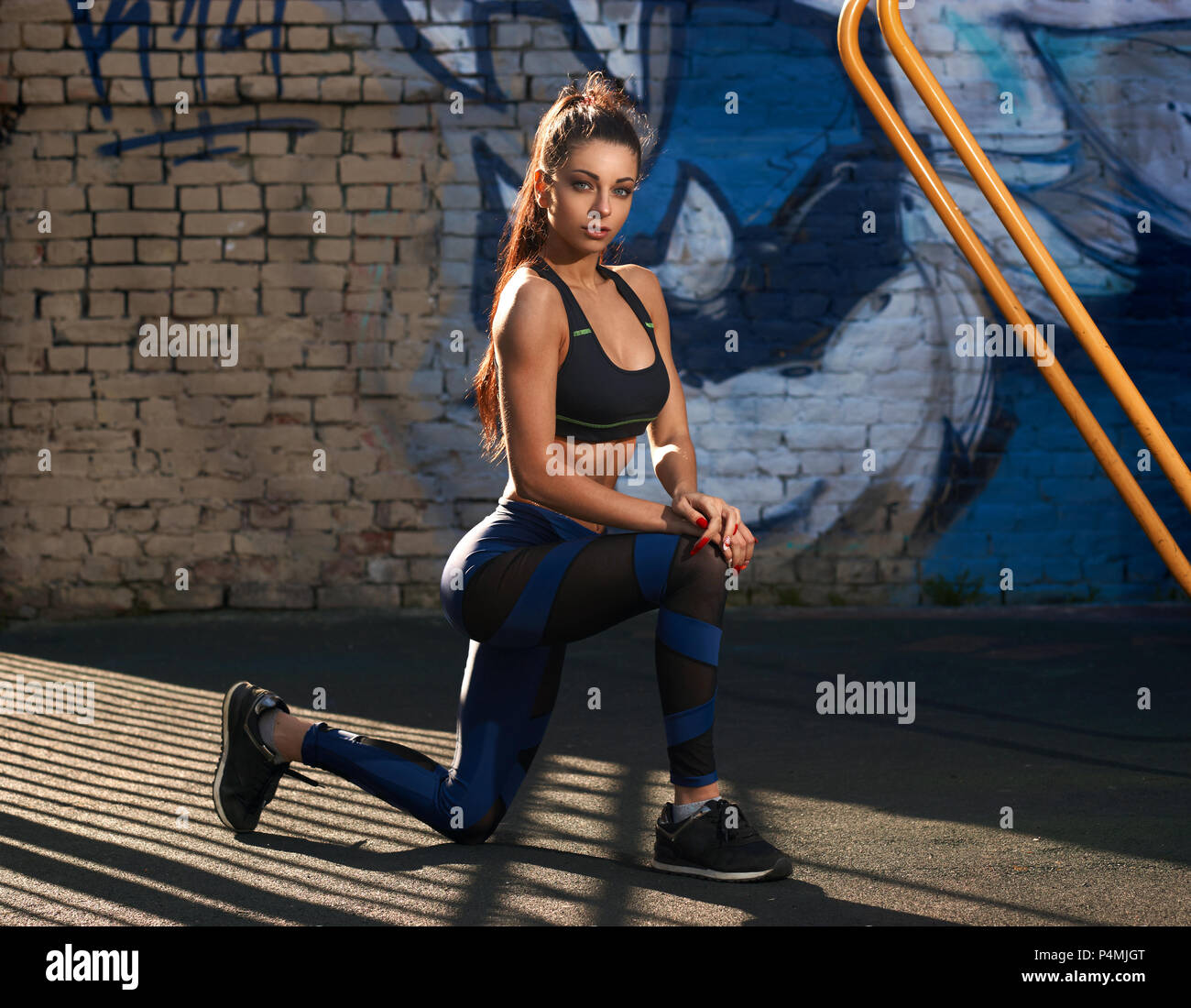 Beautiful young woman with long legs in bright sexy leggings with pretty  athlete muscular body sit with protein shaker. Crossfit training urban area  street gym city exercise routine healthy lifestyle. Stock Photo