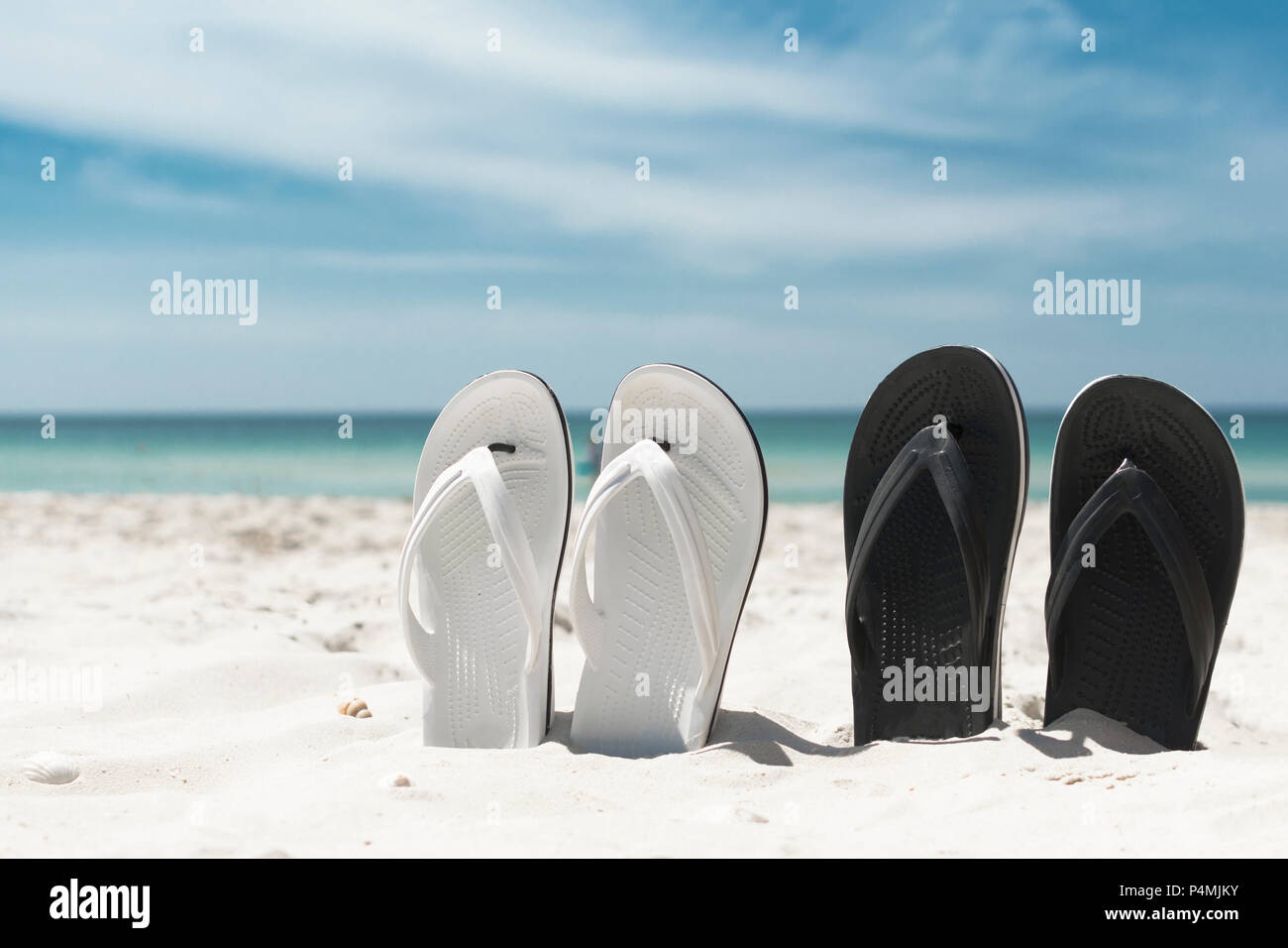 Two pair of white and blackn flip-flops in the sand. Summer vacation