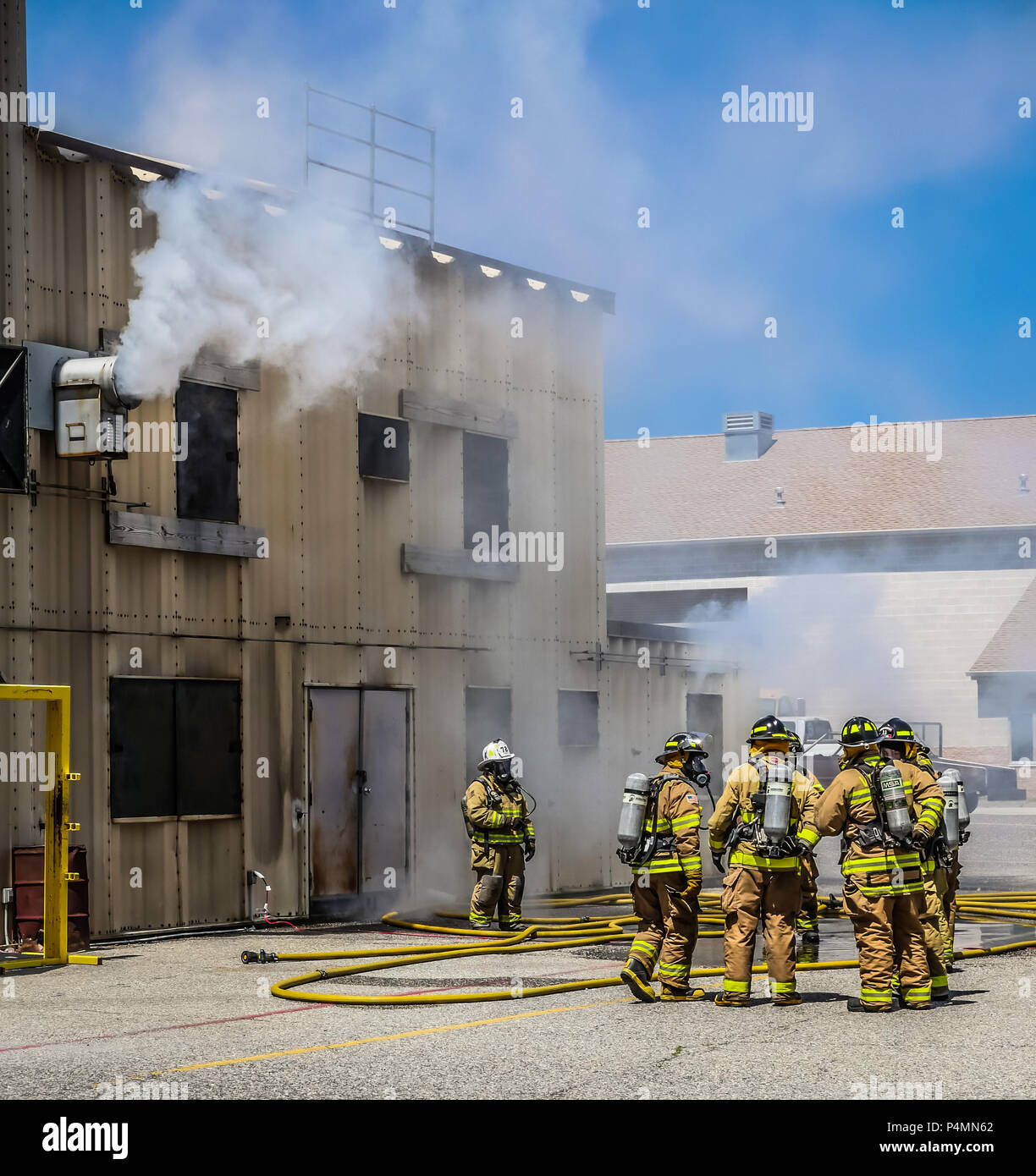 Firefighters in full turnout gear standing outside a burn building for training. Stock Photo