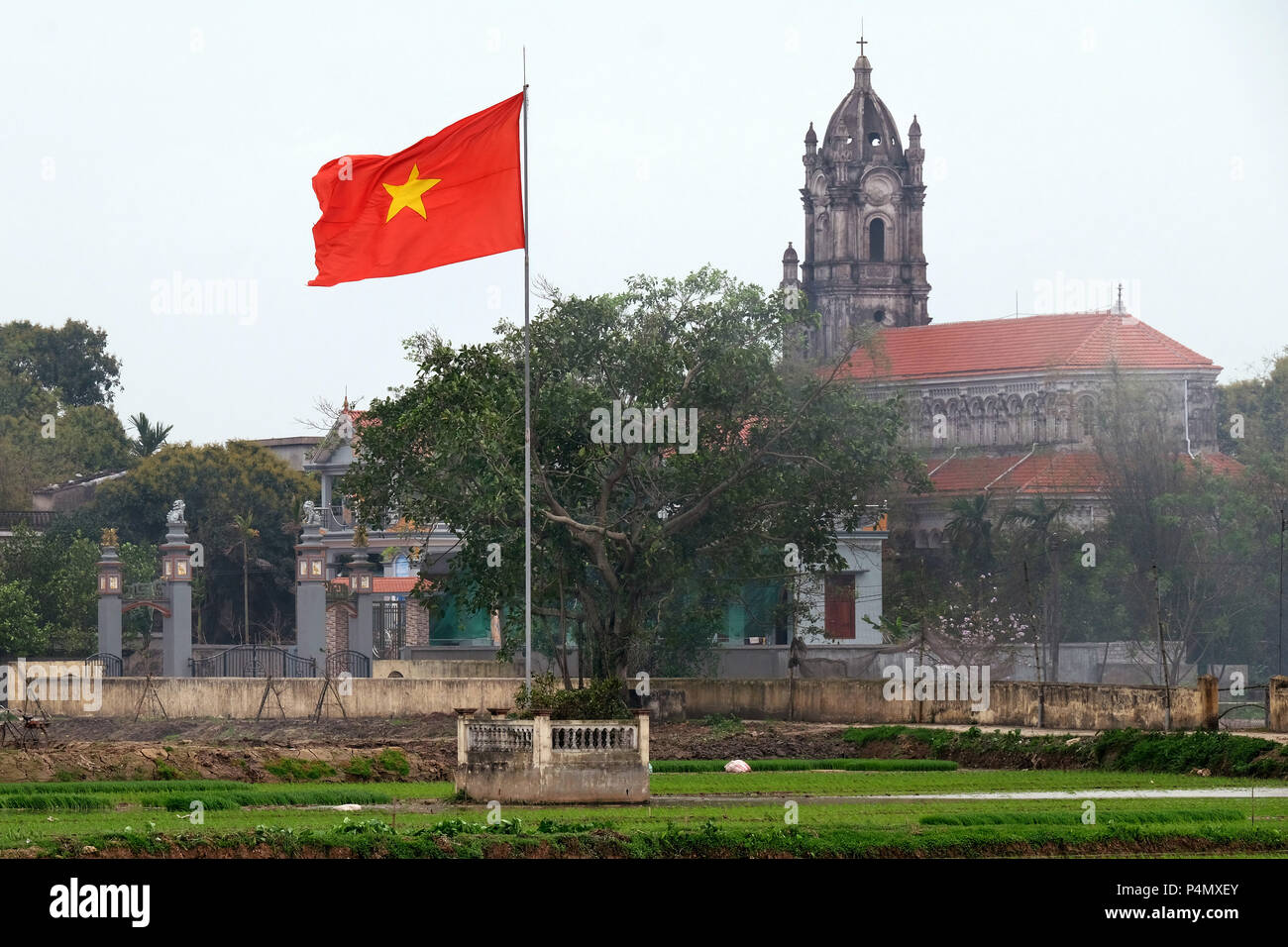 Vietnam country flag and catholic church in a rice field in Nam Dinh province, Vietnam - Landesfahne Vietnams und katholische Kirche in einem Reisfeld in der Nam Dinh-Provinz, Vietnam Stock Photo
